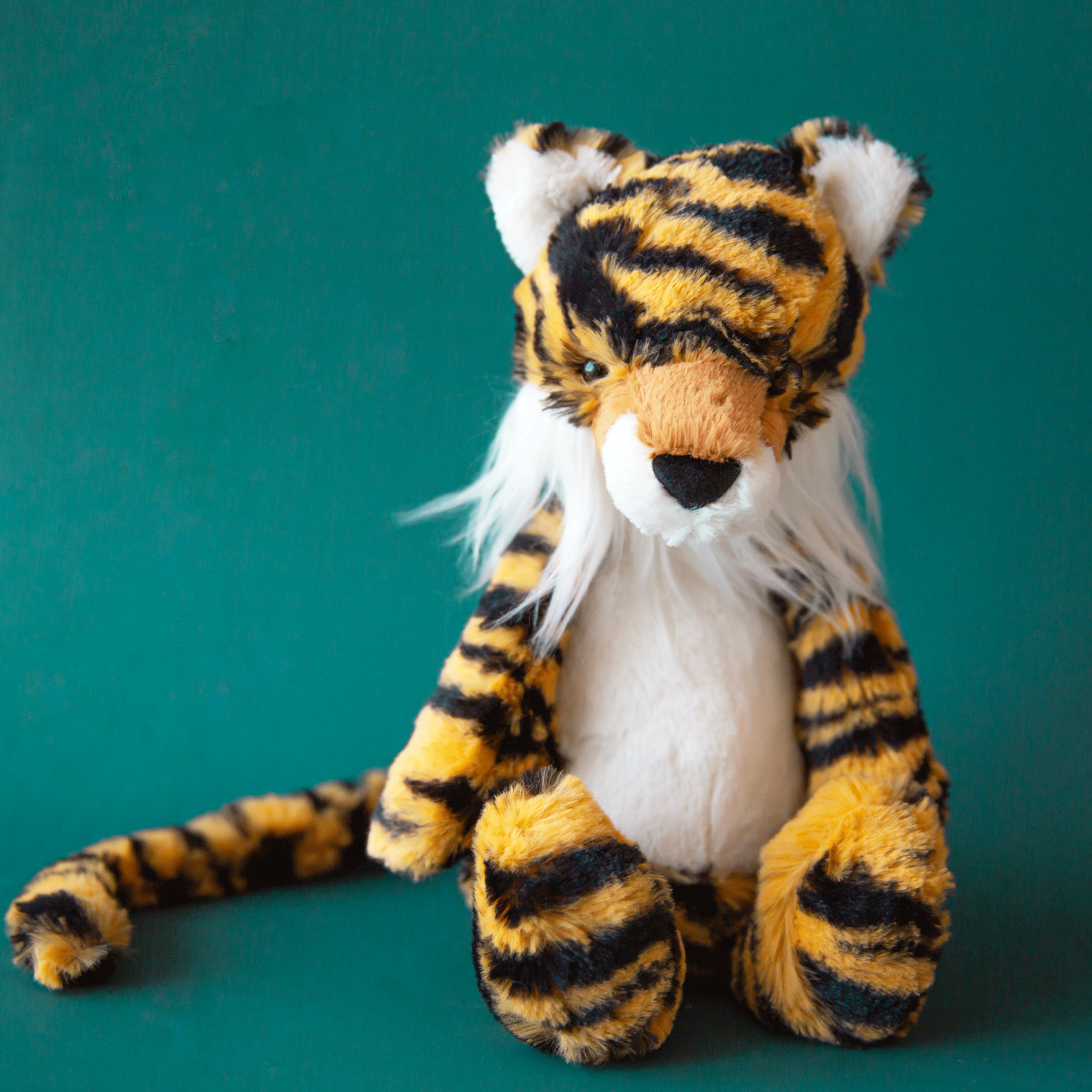 On a teal background is a orange and black striped tiger stuffed toy. 