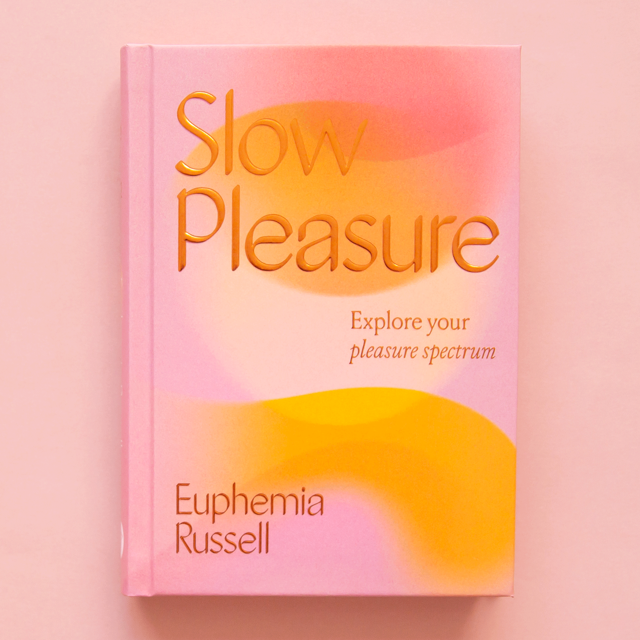 On a pink background is a orange and pink book that reads, &quot;Slow Pleasure Explore your pleasure spectrum&quot;. 