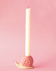 On a pink background is a ceramic pink snail shaped candle holder.