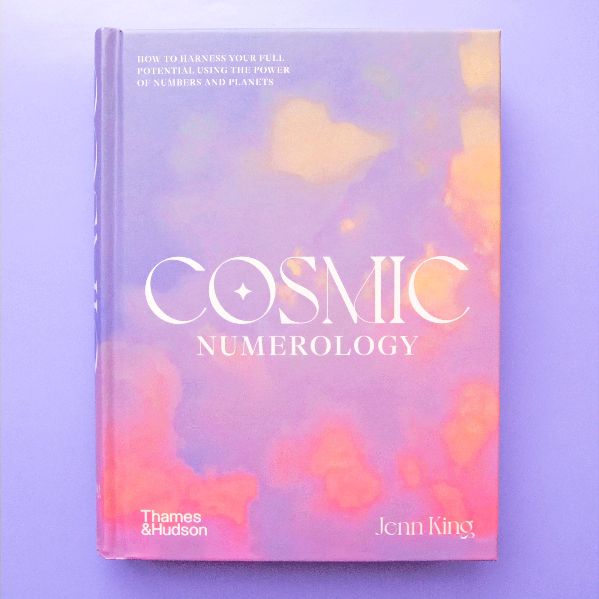 On a purple background is a purple and pink sunset book cover with white text in the center that reads, &quot;Cosmic Numerology&quot;. 