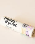 On a tan background is an ivory lip balm with black text that reads, "poppy & pout Pina colada".