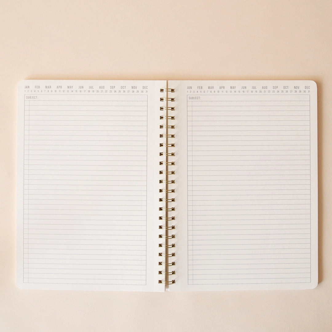 On a beige background is the spiral notebook opened showing the lined pages on the interior of the notebook along with all the months and days at the top so the user can select any day. 