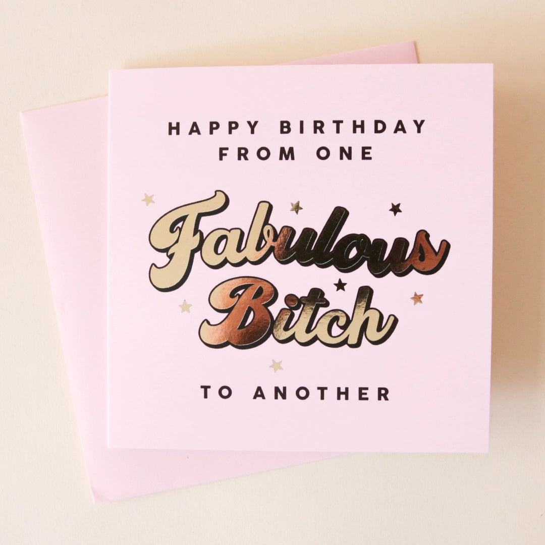 A light pink 5"x7" card that reads, "Happy Birthday From One Fabulous Bitch To Another" in gold font. The card is also pictured with its bright pink envelope that is included.