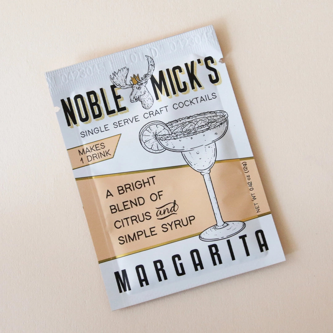 A tangerine and white packet of margarita mix with the title, "Noble Mick's Single Serve Craft Cocktails" along with a drawing of a margarita and their mascot which is a moose