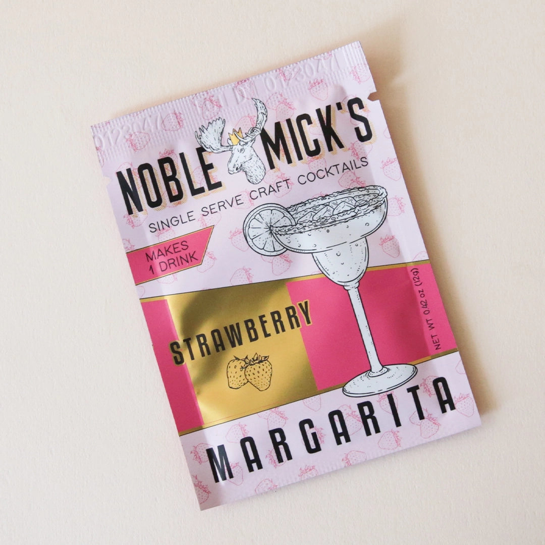 On a white background is a hot pink and light pink packet of cocktail mix that reads, "Noble Micks Single Serve Craft Cocktails Strawberry Margarita".