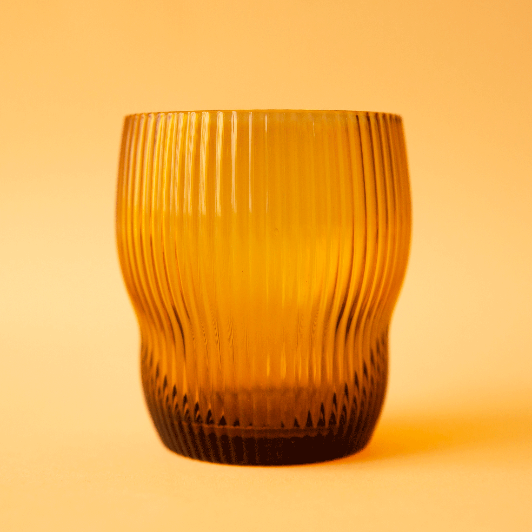 On a orange background is a fluted drinking glass in an amber color. 