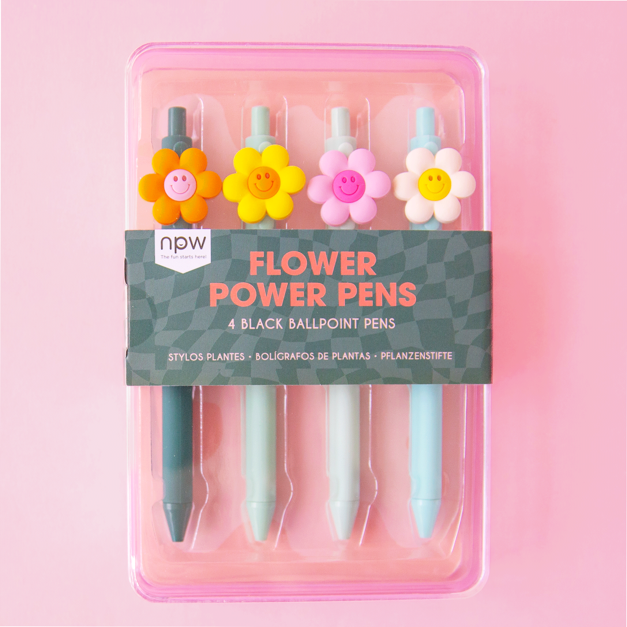 On a pink background is a set of four ballpoint pens with a 3D smiley face daisy on each one in a different color. The pens themselves range between shades of light blue and teal. 