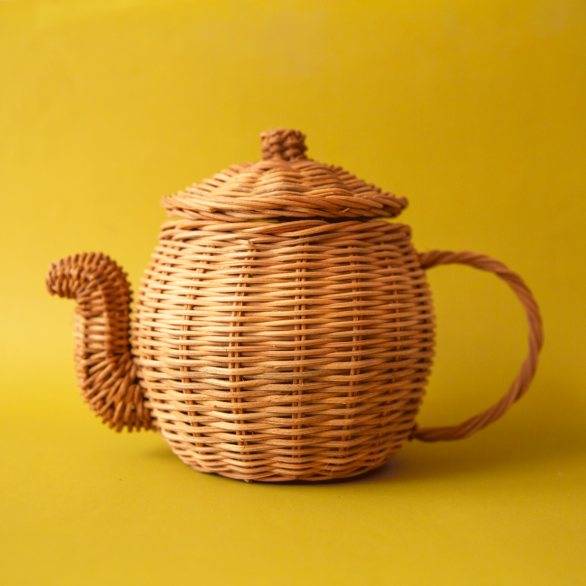 On a chartreuse background is a rattan tea pot and rattan tea cup, saucer and spoon