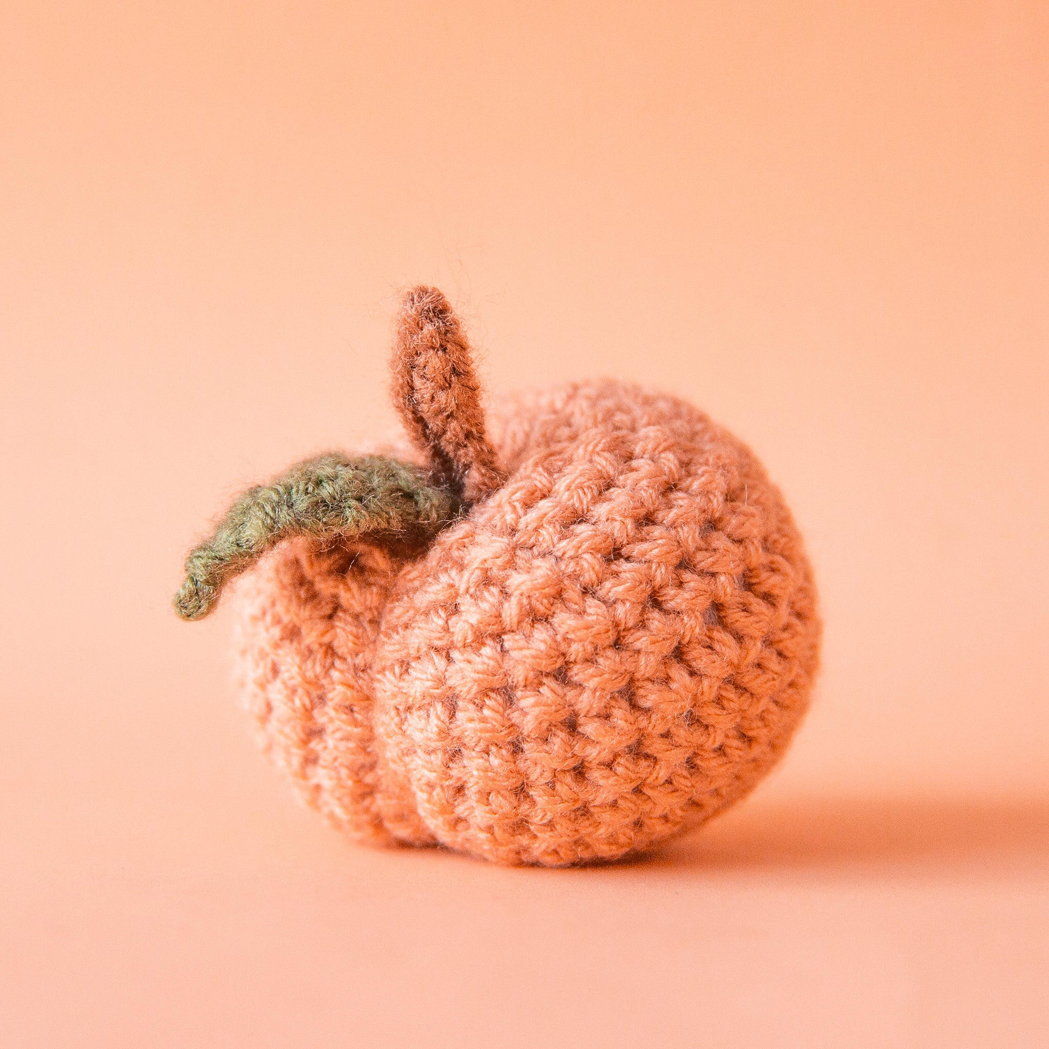On a peachy background is a knitted peach shaped toy.
