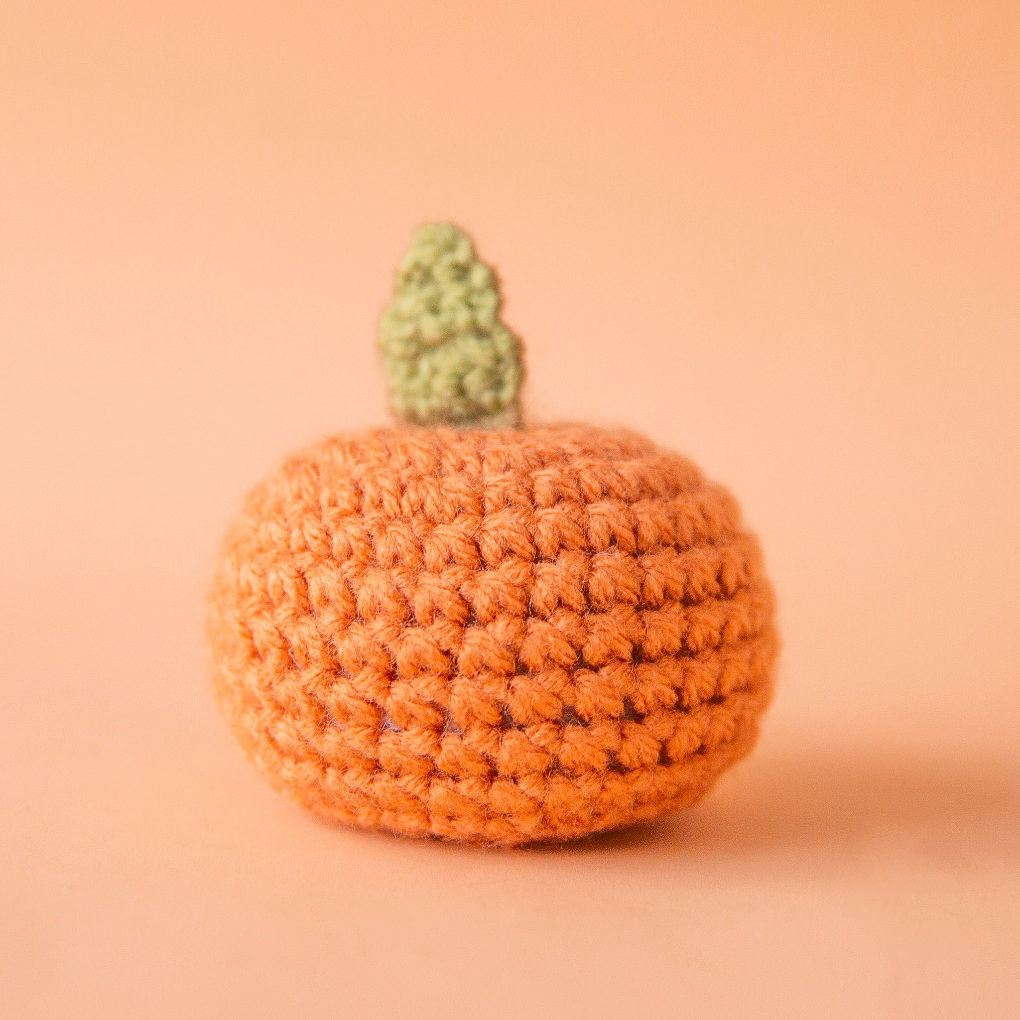 On a peachy background is a knitted orange shaped toy. 