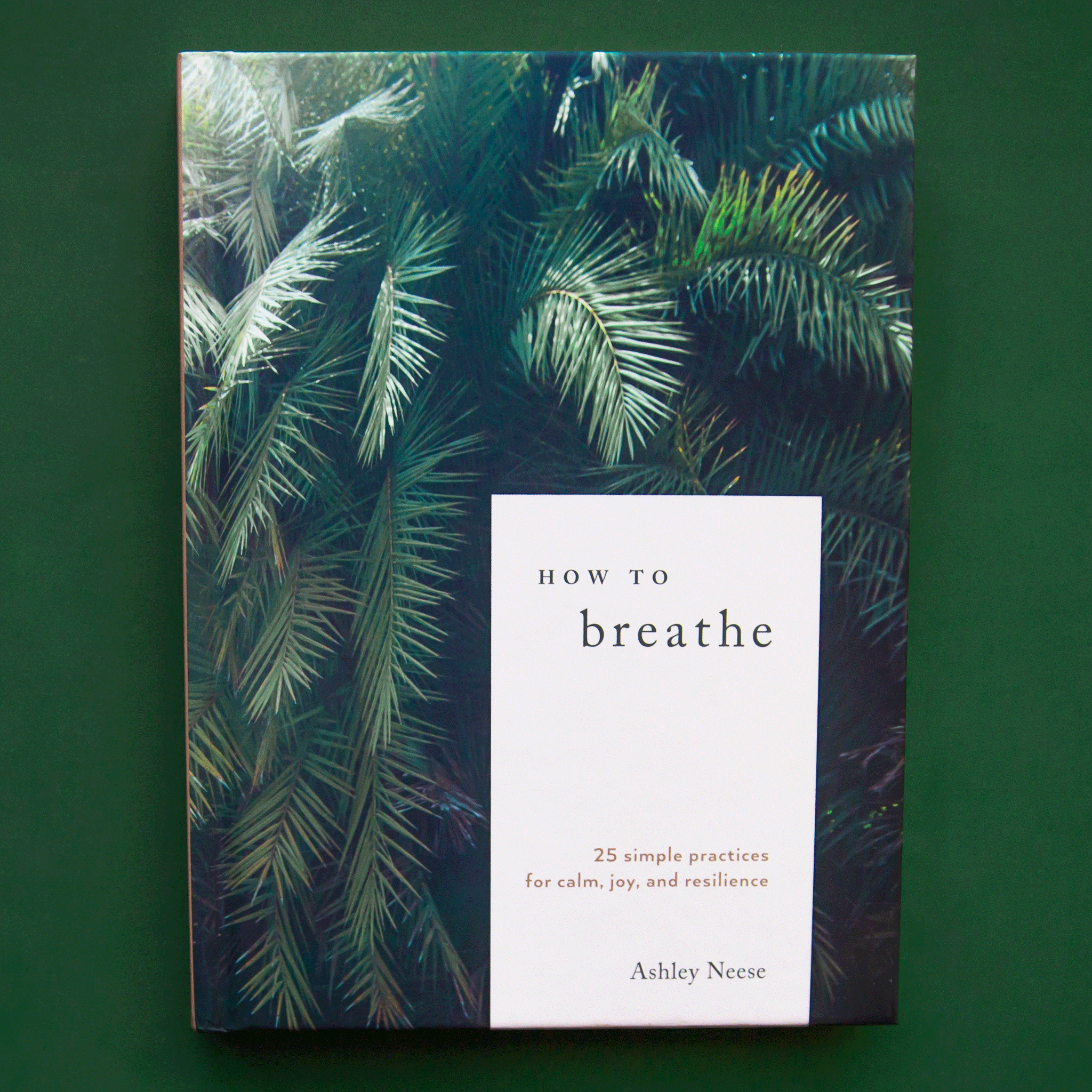 A hardcover book with green palms with a white rectangle in the bottom right hand corner of the front cover that reads, &quot;How to Breathe 25 simple practices for calm, joy and resilience, Ashley Neese&quot;.