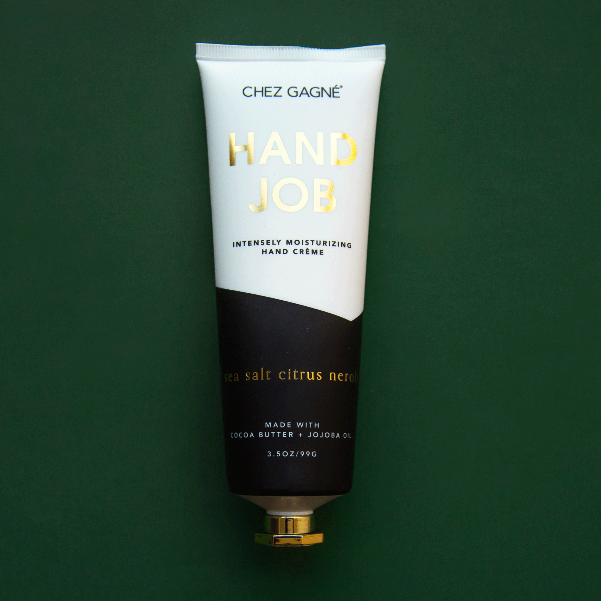 On a dark green  background is a tube of hand cream that is half black and half white along with gold text that reads, &quot;Hand Job&quot; as well as black text underneath that reads, &quot;Intensely moisturizing hand crème.