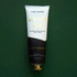 On a dark green  background is a tube of hand cream that is half black and half white along with gold text that reads, "Hand Job" as well as black text underneath that reads, "Intensely moisturizing hand crème.