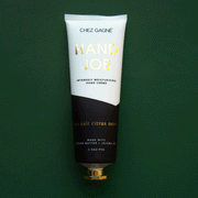 On a dark green background is a tube of hand cream that is half black and half white along with gold text that reads, "Hand Job" as well as black text underneath that reads, "Intensely moisturizing hand crème.
