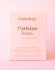 On a pink background is a pink clay jarred candle with a lid and the box that it comes in on the side that reads, "Parisian Rose for mind body and soul.".
