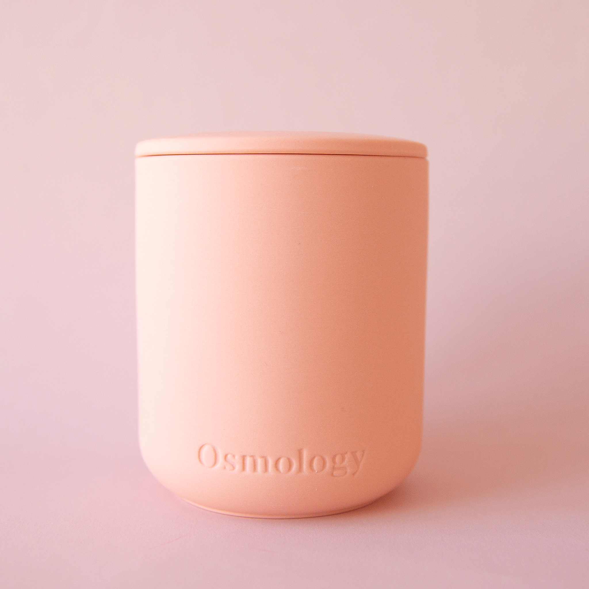 On a pink background is a peach clay candle with a lid.