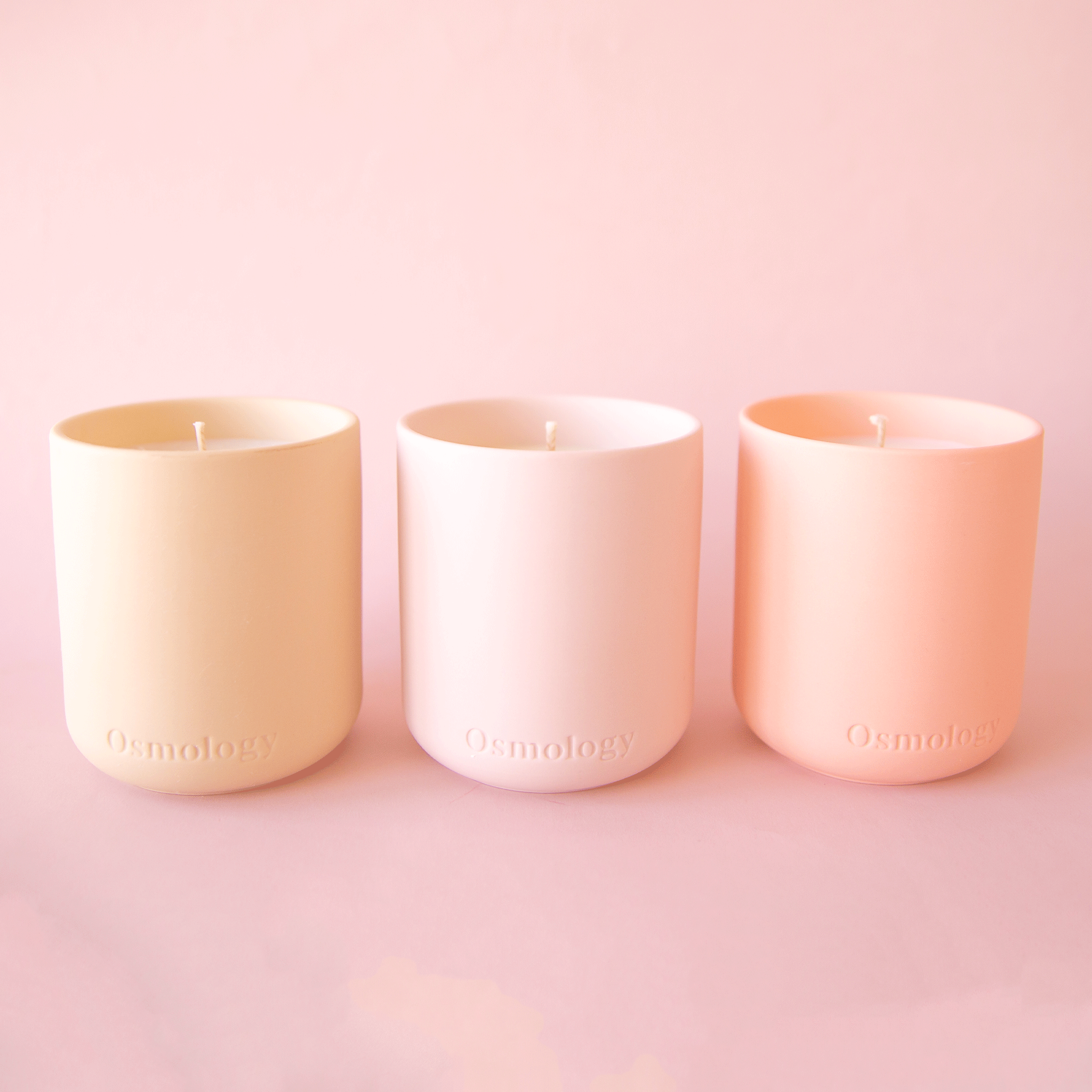 On a pink background is three clay candles in shades of peach and pink.
