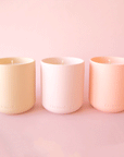 On a pink background is three clay candles in shades of peach and pink.