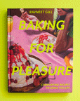 On a green background is a hot pink book cover with desserts on the front and yellow text that reads, "Baking For Pleasure".