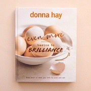 On a tan background is a neutral book cover with a photo of a bowl of eggs and the title that reads, "even more basics to Brilliance".
