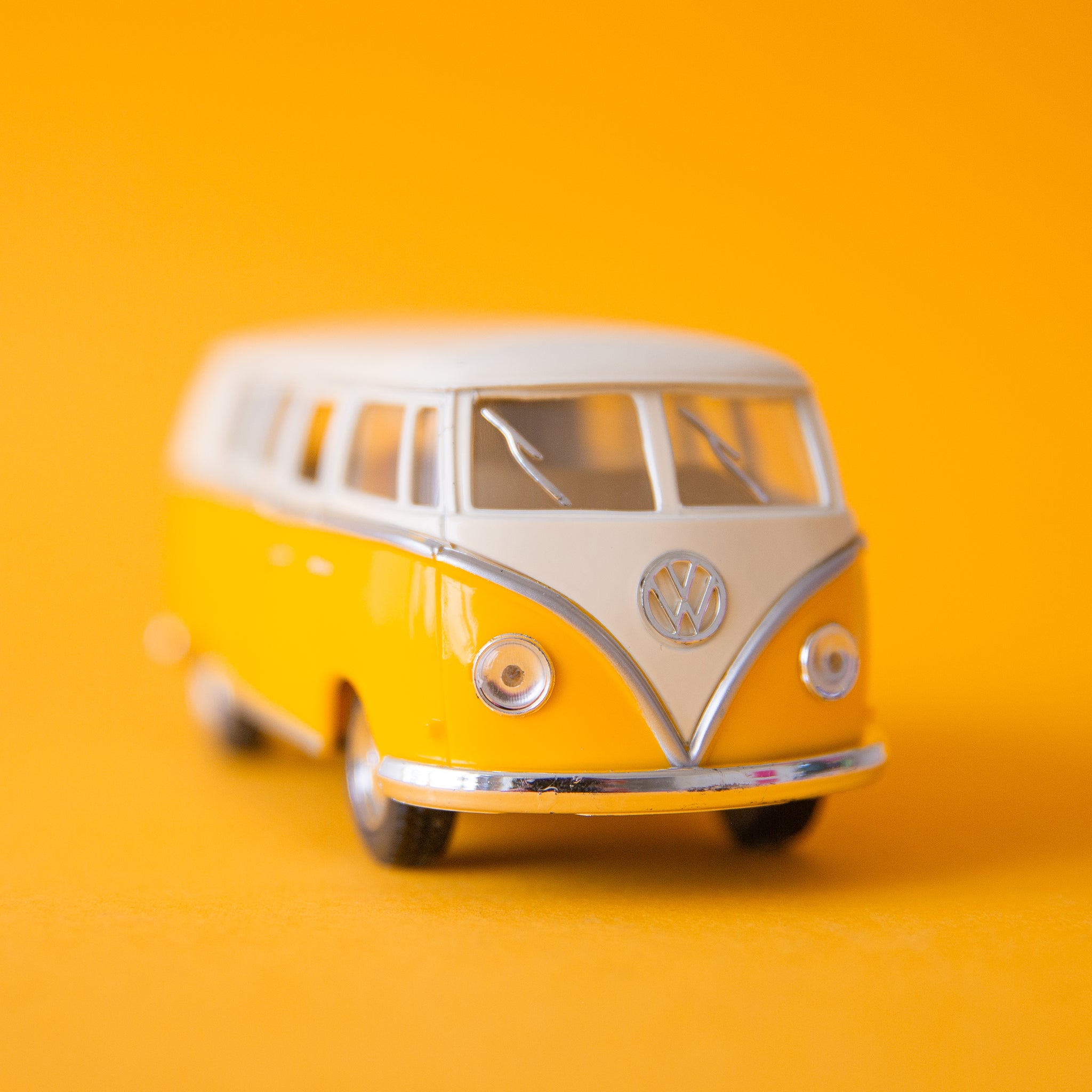 On a yellow background is a yellow and white VW bus toy. 