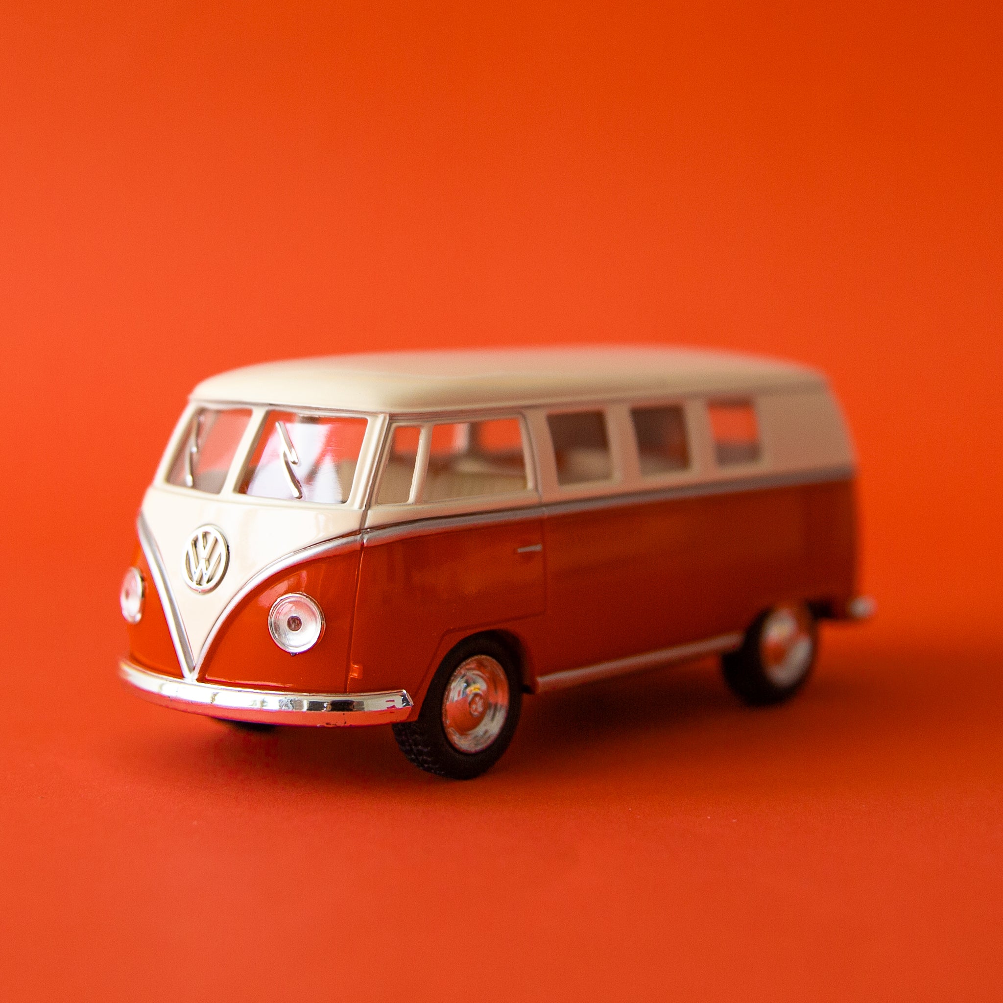 On a red background is a red and white VW bus toy. 