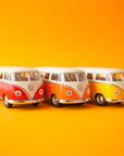 On a yellow background is three volkswagen bus toys in a red shade, an orange and a yellow. Each color sold separately.