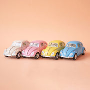 On a tan background is all four toy Volkswagen Beetle cars in a white, pink, yellow and blue color.