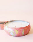 A round tin 3 wick candle with an abstract floral and spotted design. The metal from the tin reflects light in a beautiful way, especially on its gold parts. The other colors on this tin are white and and a peach color.