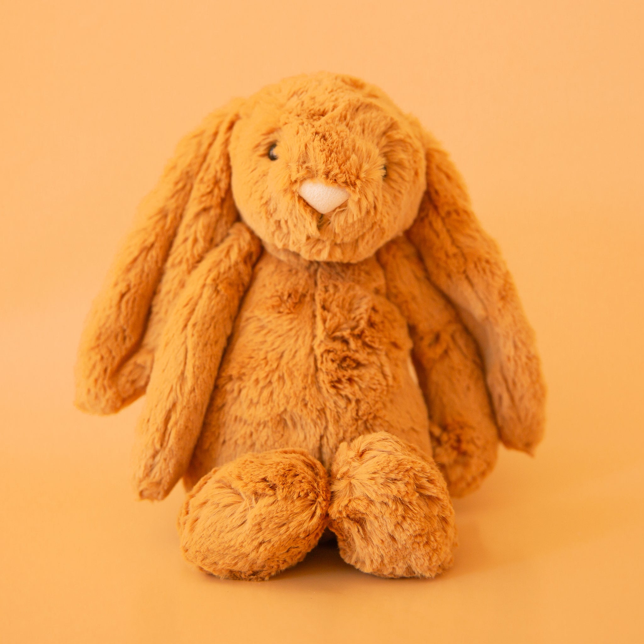 On a orange background is a golden yellow furry bunny stuffed animal toy. 