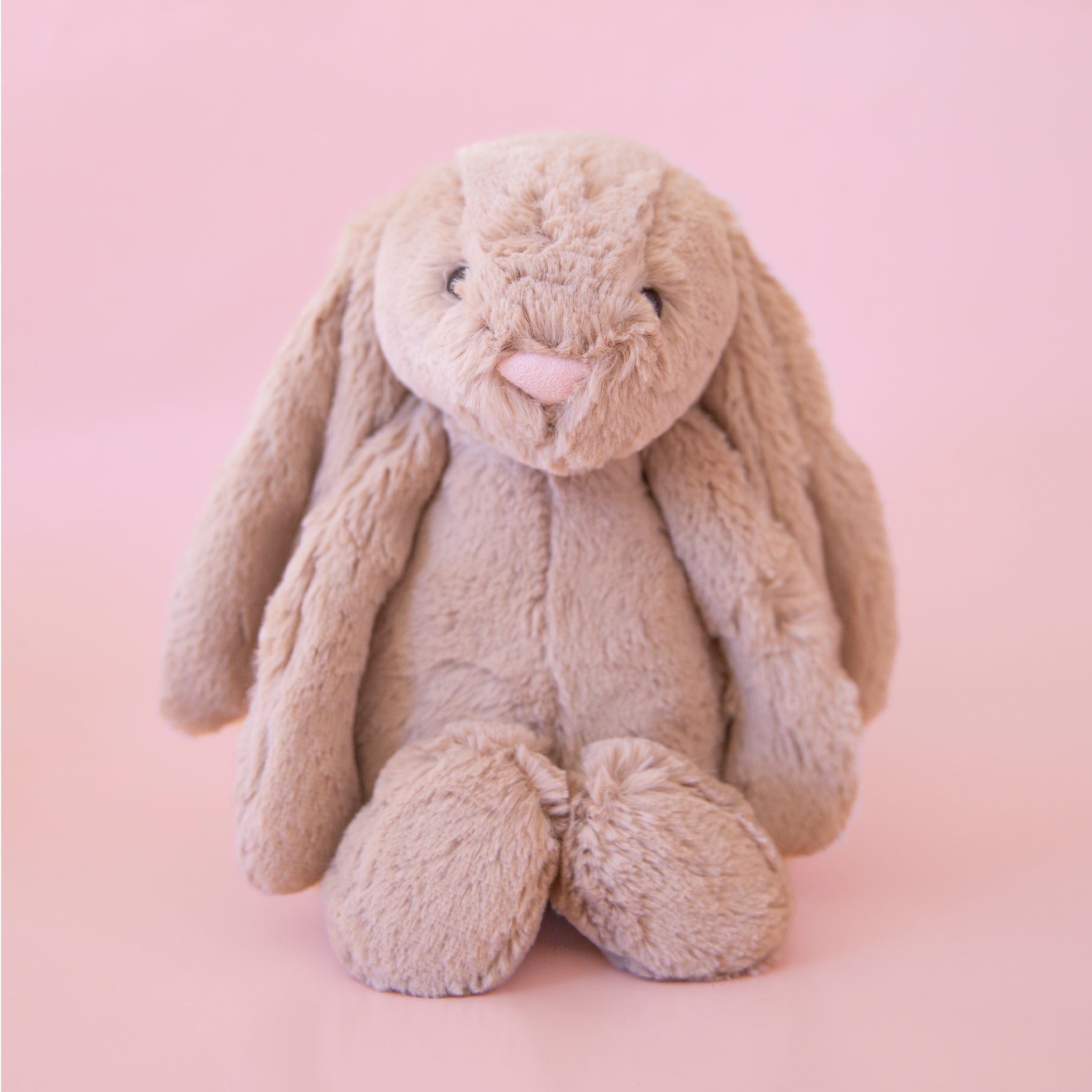 Soft stuffed animal in the shape of a beige-grey colored rabbit, with long floppy ears, arms and legs.