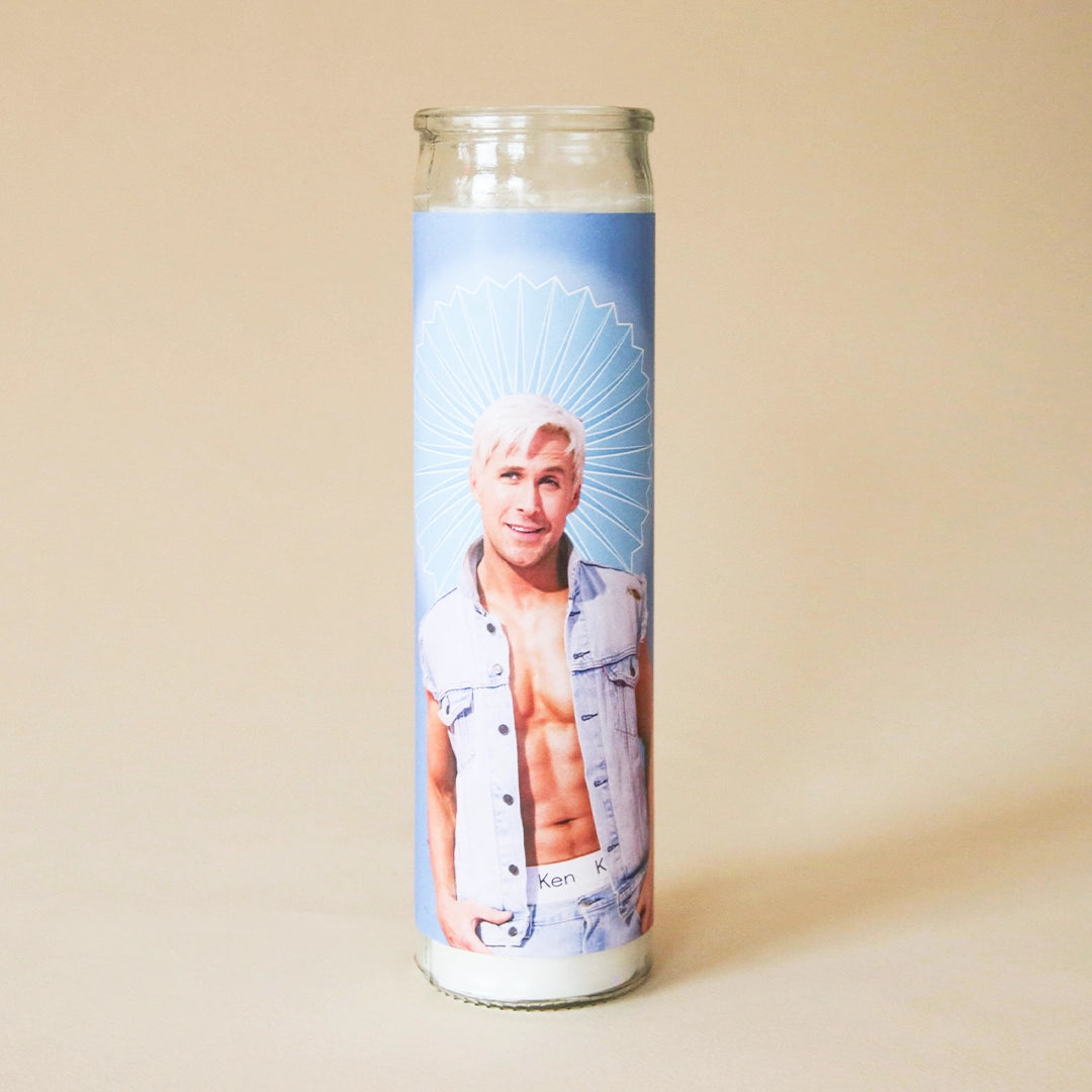 On a tan background is a blue prayer candle with a photo of Ken played by the actor Ryan Gosling. 