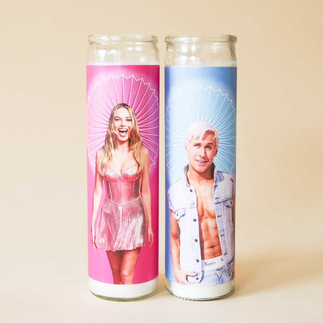 On a tan background is a blue prayer candle with a photo of Ken played by the actor Ryan Gosling and sitting next to another prayer candle available on our site featuring Barbie. 