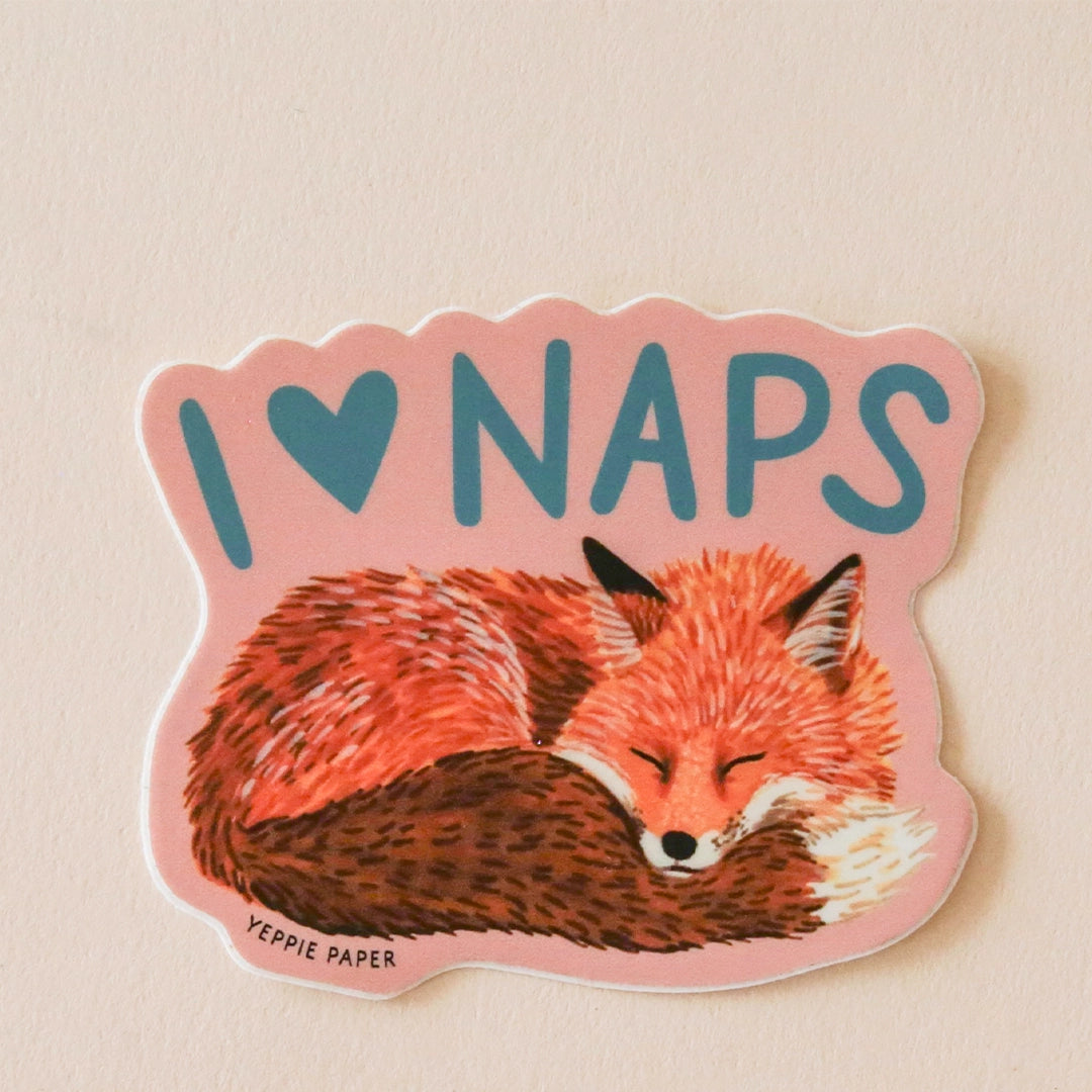 almon colored. sticker with an illustration of a sleeping fox and turquoise blue text above it that reads, "I heart Naps".