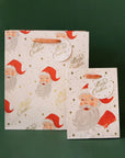 Two different sized ivory gift bags with a red Santa design along with gold text that reads, "Merry Christmas".
