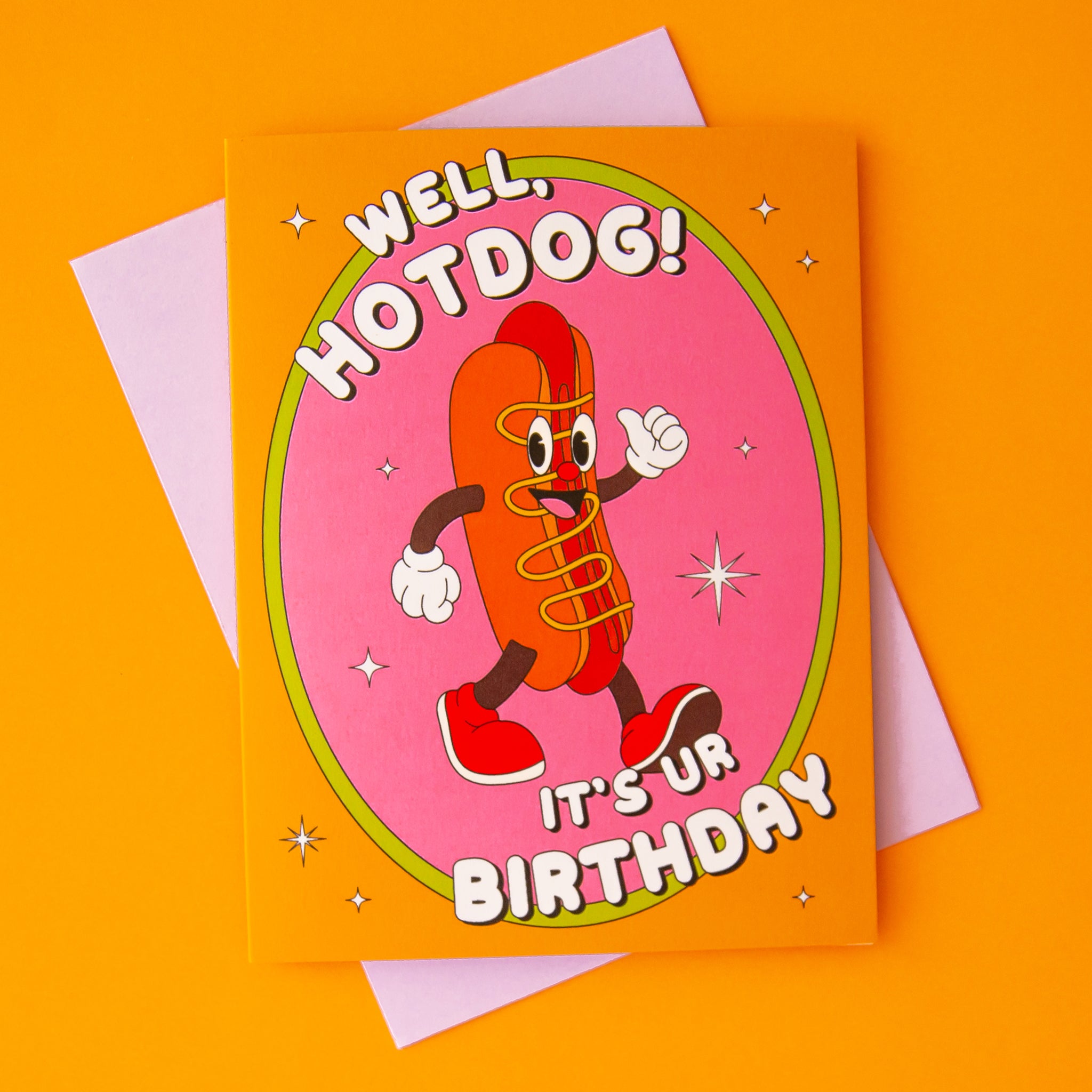 On an orange background is an orange and pink card with an illustration of a smiley face hot dog with text above and below that reads, "Well, Hotdog! It's Ur Birthday". 