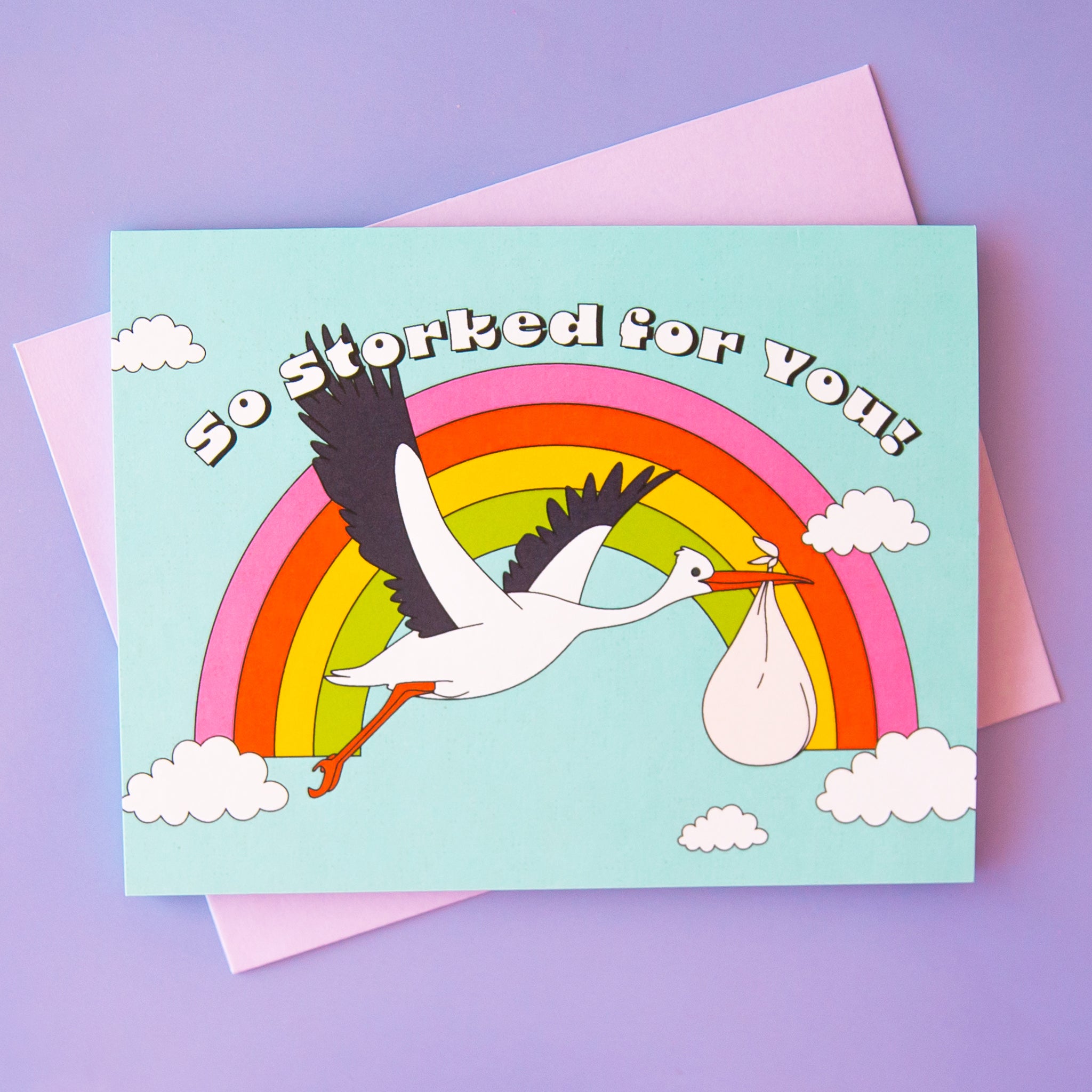 On a purple background is a blue card with imagery of a rainbow and a flying stork holding a white sack and text above that reads, &quot;So Storked For You!&quot;. 
