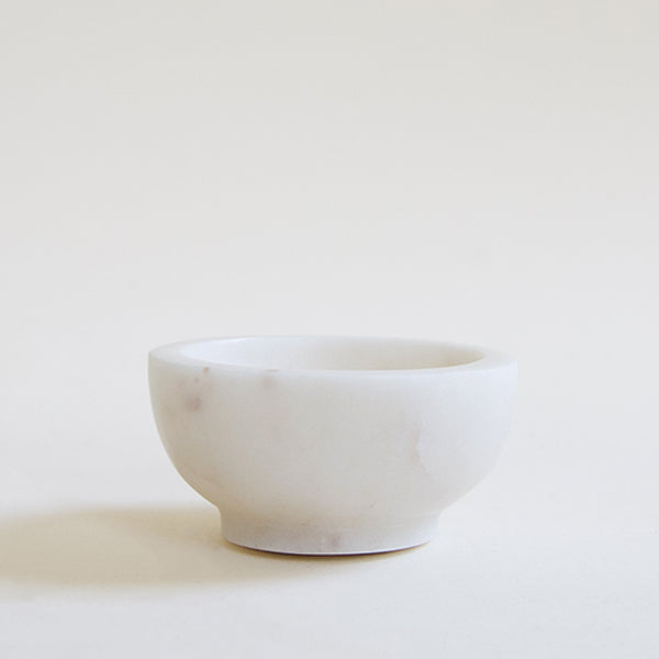 On a cream background is a small white marble bowl. 