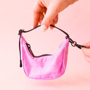 A small crescent bag charm in a pink shade with black straps and zipper.