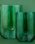 On a green background is two emerald green arched shaped glass vases. Each vase sold separately.