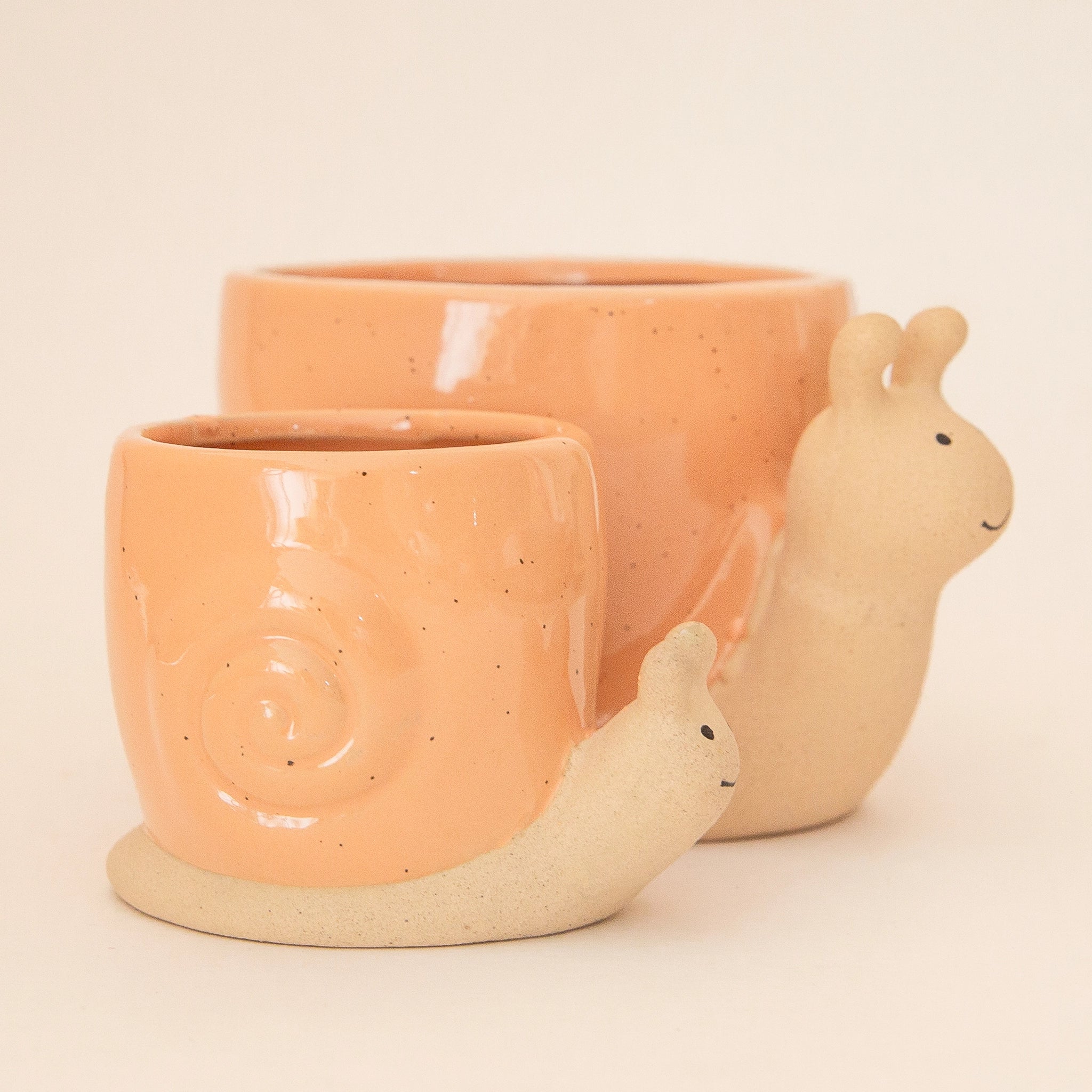 On a light peach background is two ceramic planters in the shape of a snail with a swirly light orange &quot;shell&quot;. 