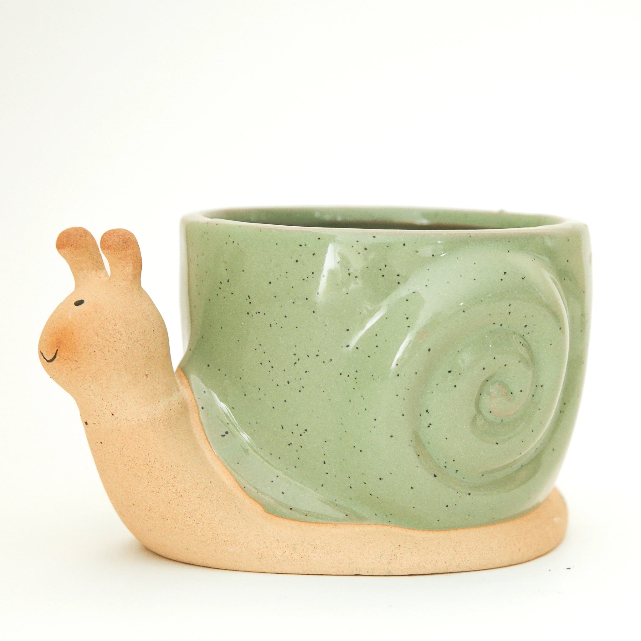On a tan background is a ceramic planter in the shape of a snail with smiling face and a swirly green &quot;shell&quot;.