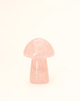 On a cream background is a model holding a tiny rose quartz crystal in the shape of a mushroom.