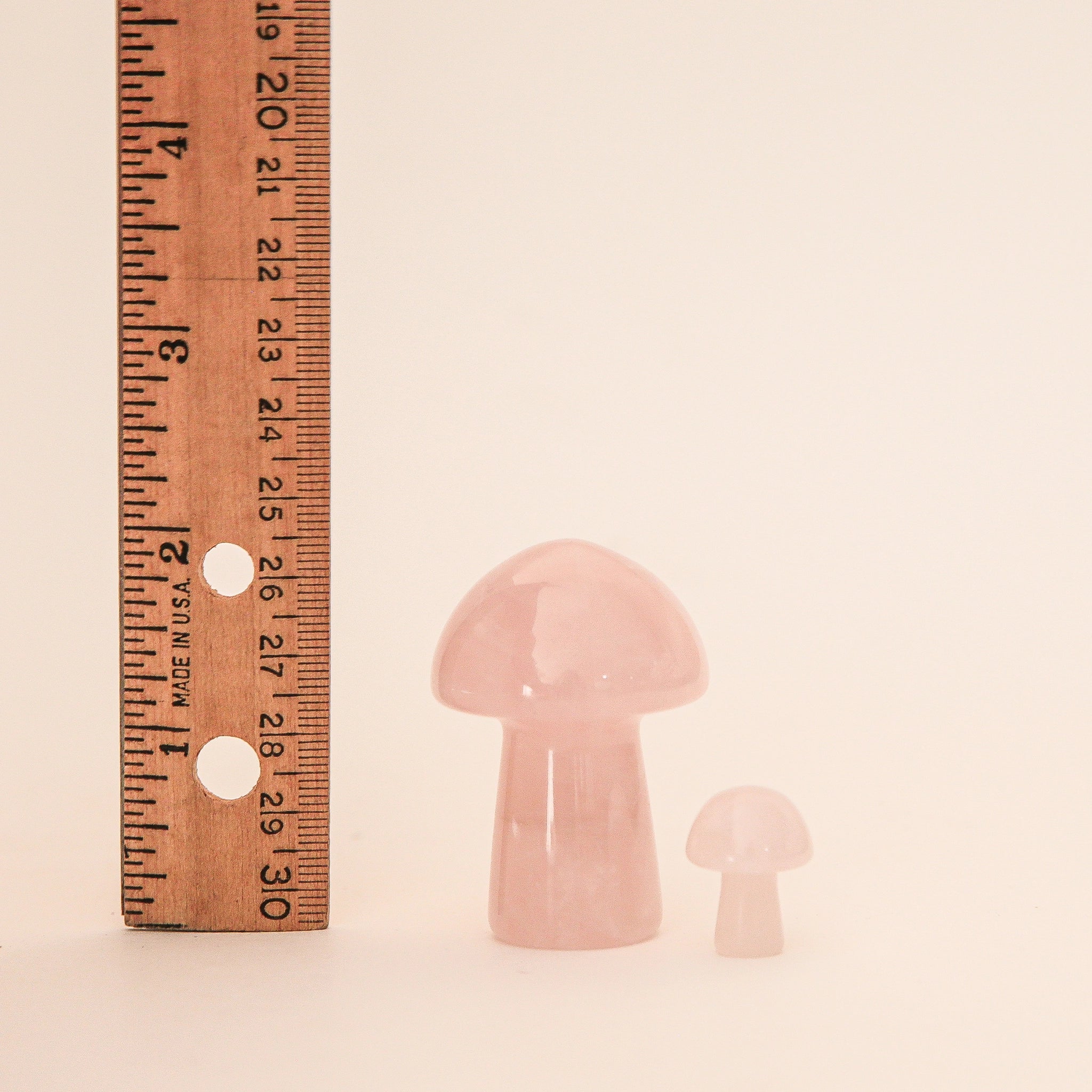 On a tan background is the larger rose quartz mushroom next to the mini version along with a ruler to show the height difference. 