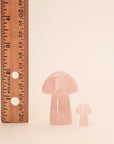 On a tan background is the larger rose quartz mushroom next to the mini version along with a ruler to show the height difference.
