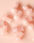 On a pink background is a handful of the rose quartz mushrooms scattered.