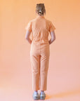 A model wearing a light peach colored short sleeve jumpsuit with a zipper up the front and a collar.