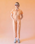 A model wearing a light peach colored short sleeve jumpsuit with a zipper up the front and a collar.