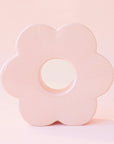 A light pink ceramic vase in the shape of a daisy with an opening in the center and an opening at the top to insert plants and floral stems.