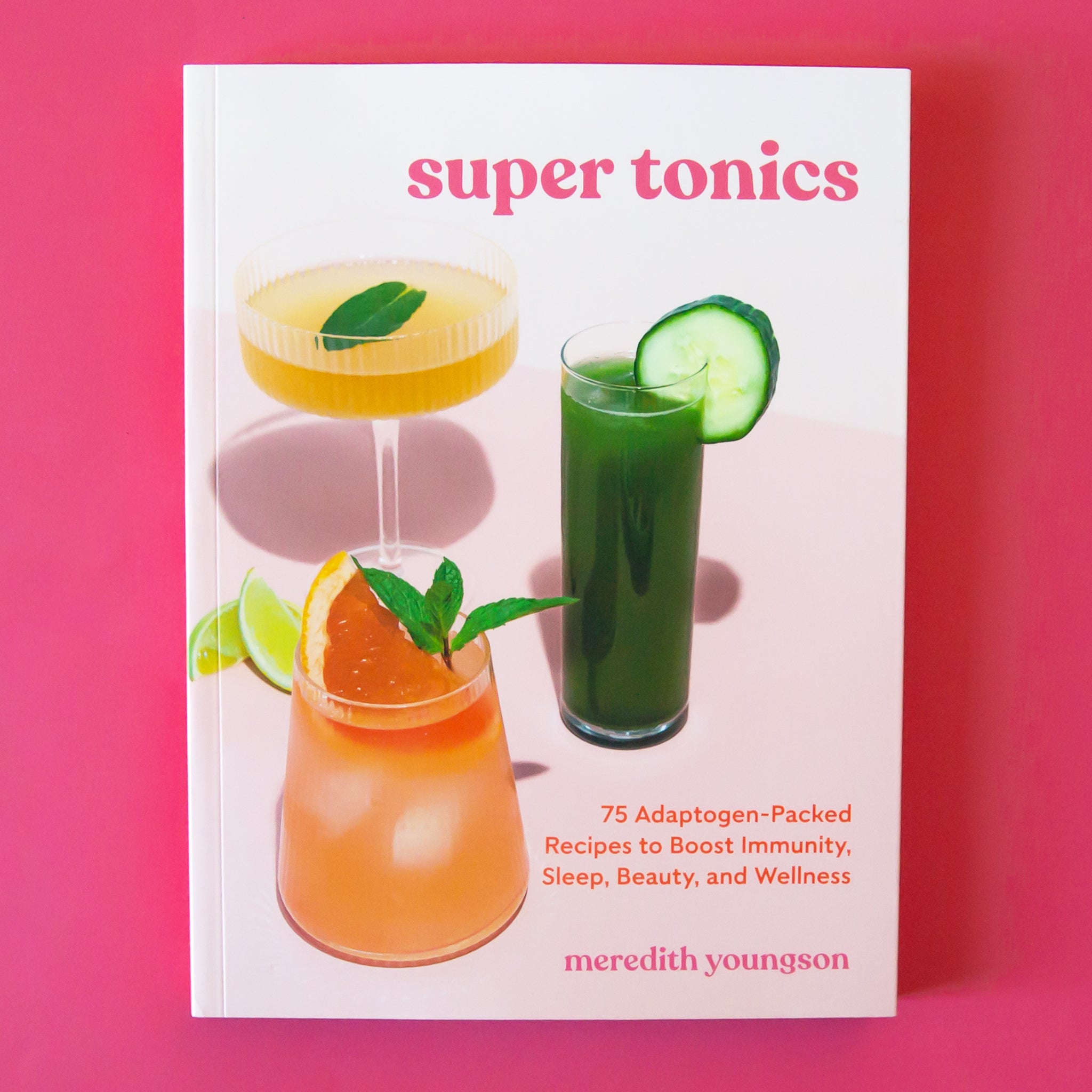 On a pink background is a book with three different drinks on the front and text that reads, "super tonics".